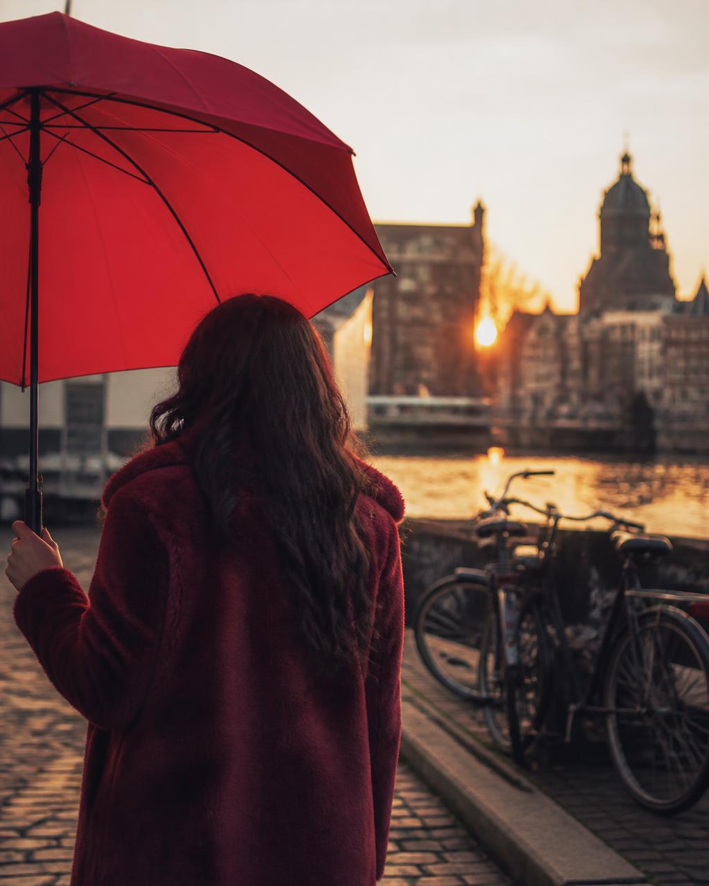 Persoon met rode paraplu bij een Amsterdamse gracht